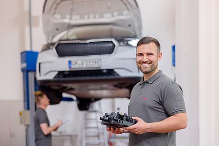 Mann mit Bauteil vor Auto in Fertigung